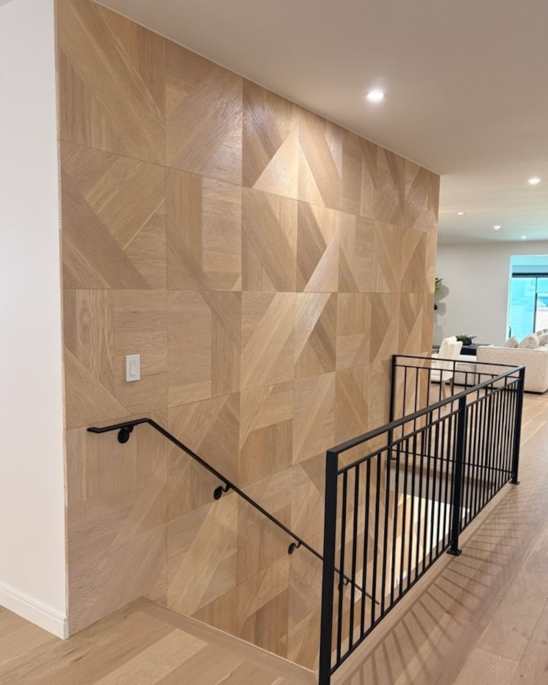 Geometric wood-look tiles covering a large accent wall next to a black metal staircase handrail.