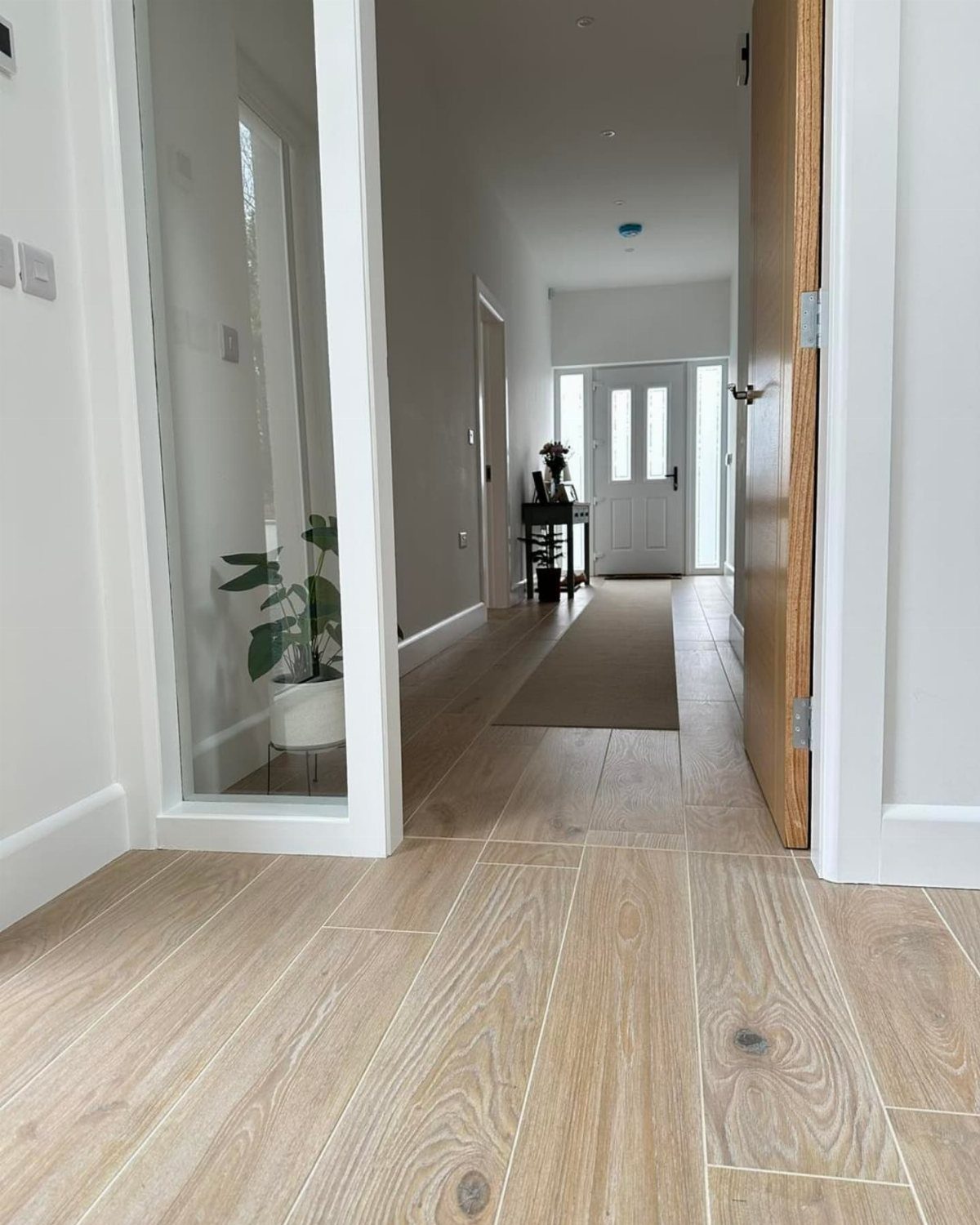 Light wood-effect floor tiles installed in a bright, modern hallway leading to a white door.