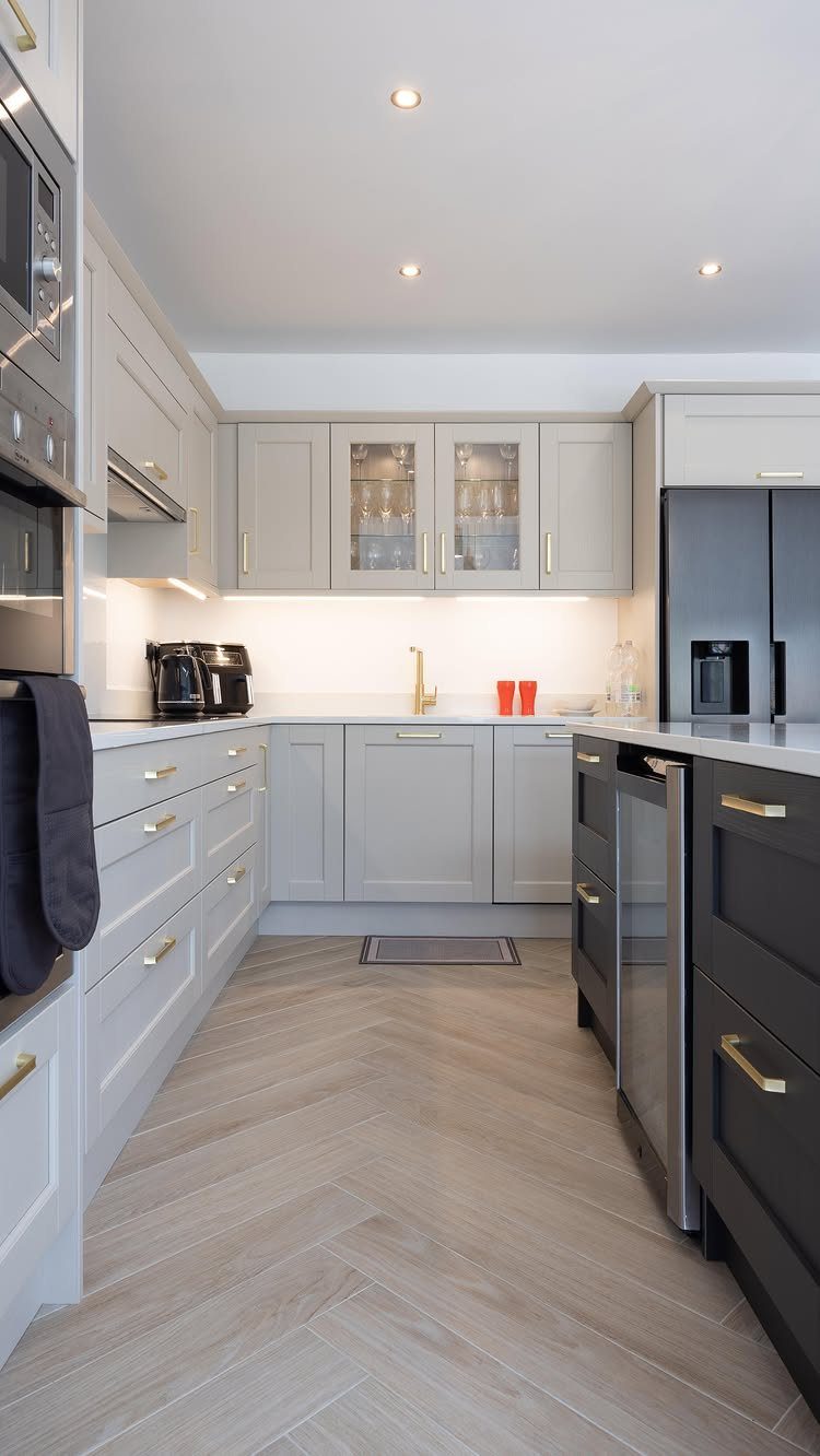 Light gray kitchen cabinets and dark island drawers with wood-look herringbone tile flooring.