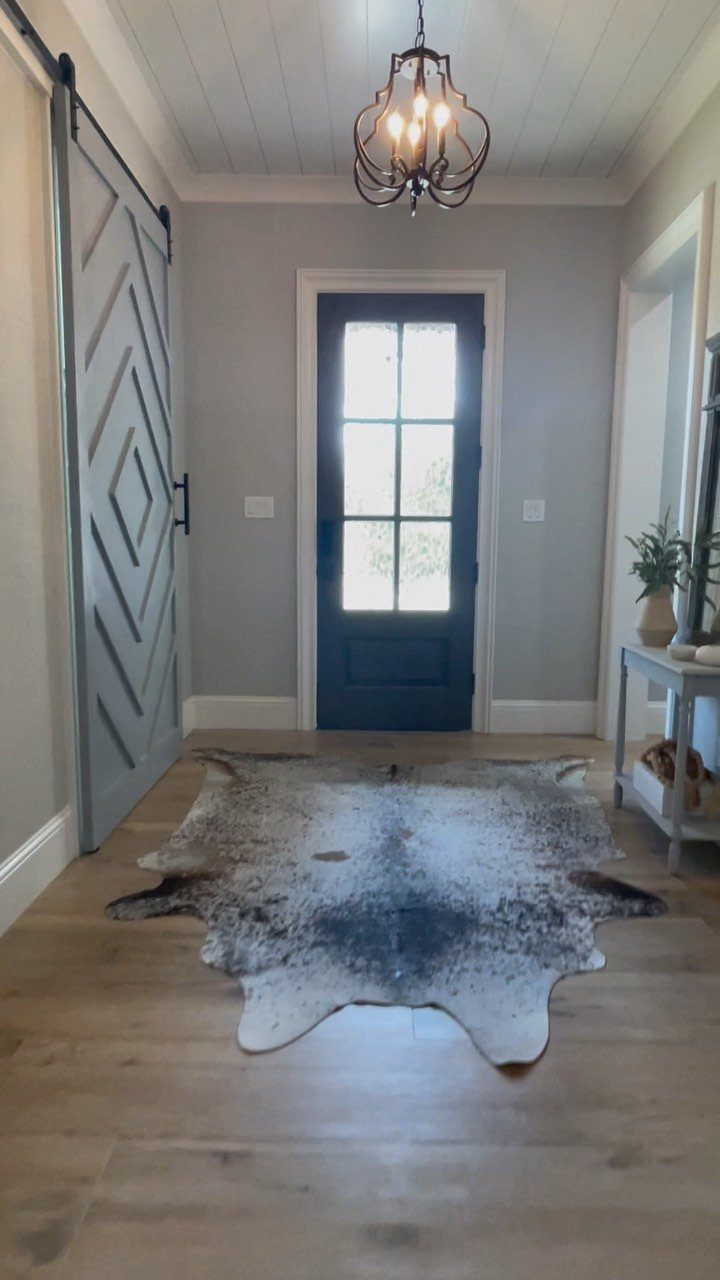 Light wood-look flooring in a hallway with a gray barn door and a cowhide rug.