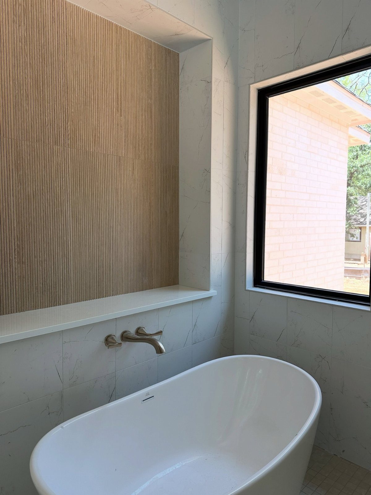 White bathtub in a bathroom with wood-look tile accents and marble-patterned walls.
