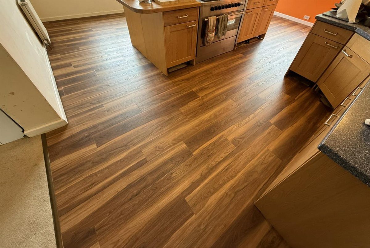 Dark wood-grain vinyl flooring installed in a kitchen with wooden cabinets and an orange wall.