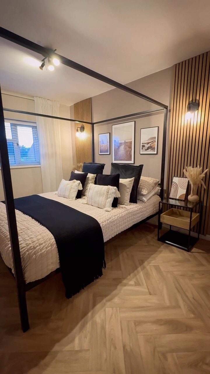 A modern bedroom with a black canopy bed and light wood-look herringbone flooring.