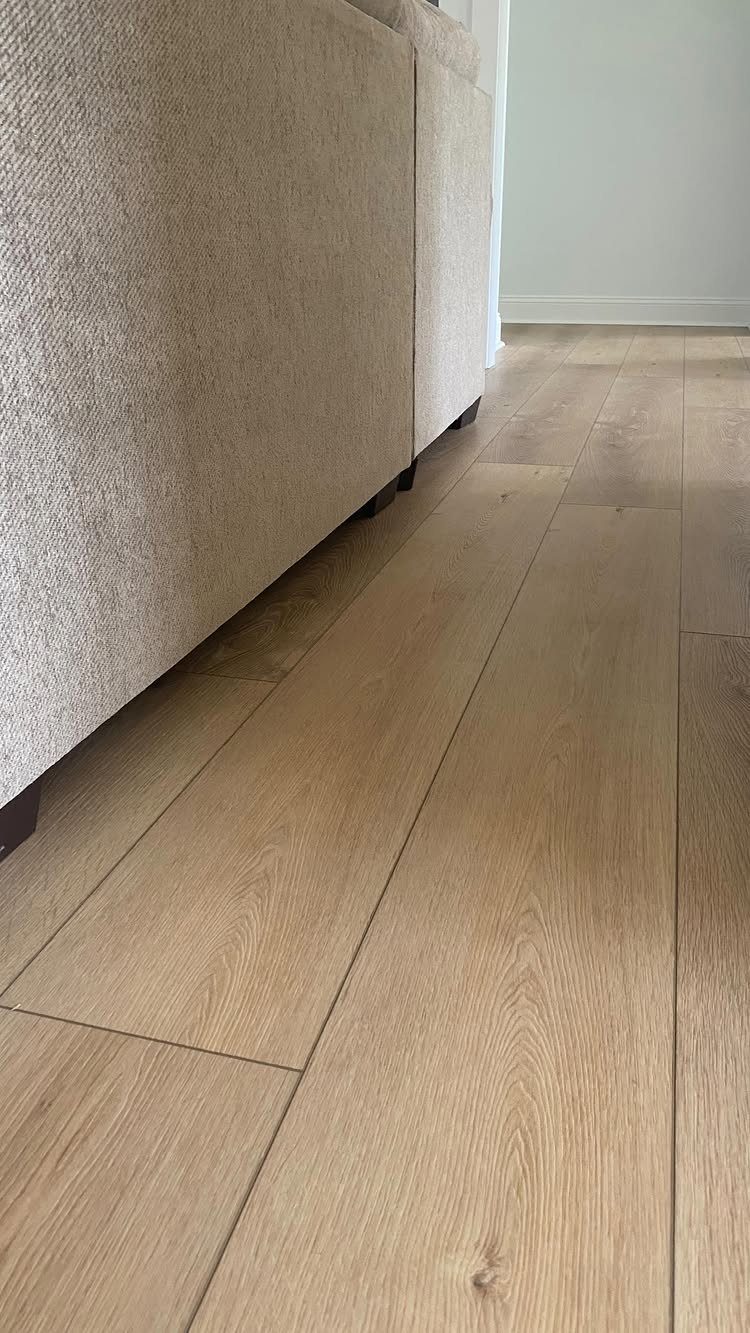 Light wood-look vinyl flooring planks installed next to a beige fabric sofa in a room.