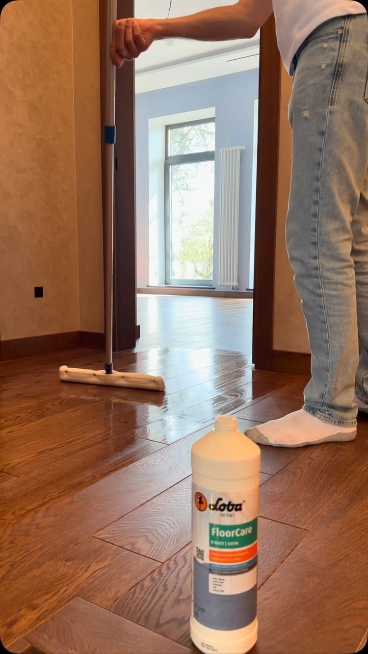 A person mopping dark oak wood flooring next to a bottle of floor care cleaner.