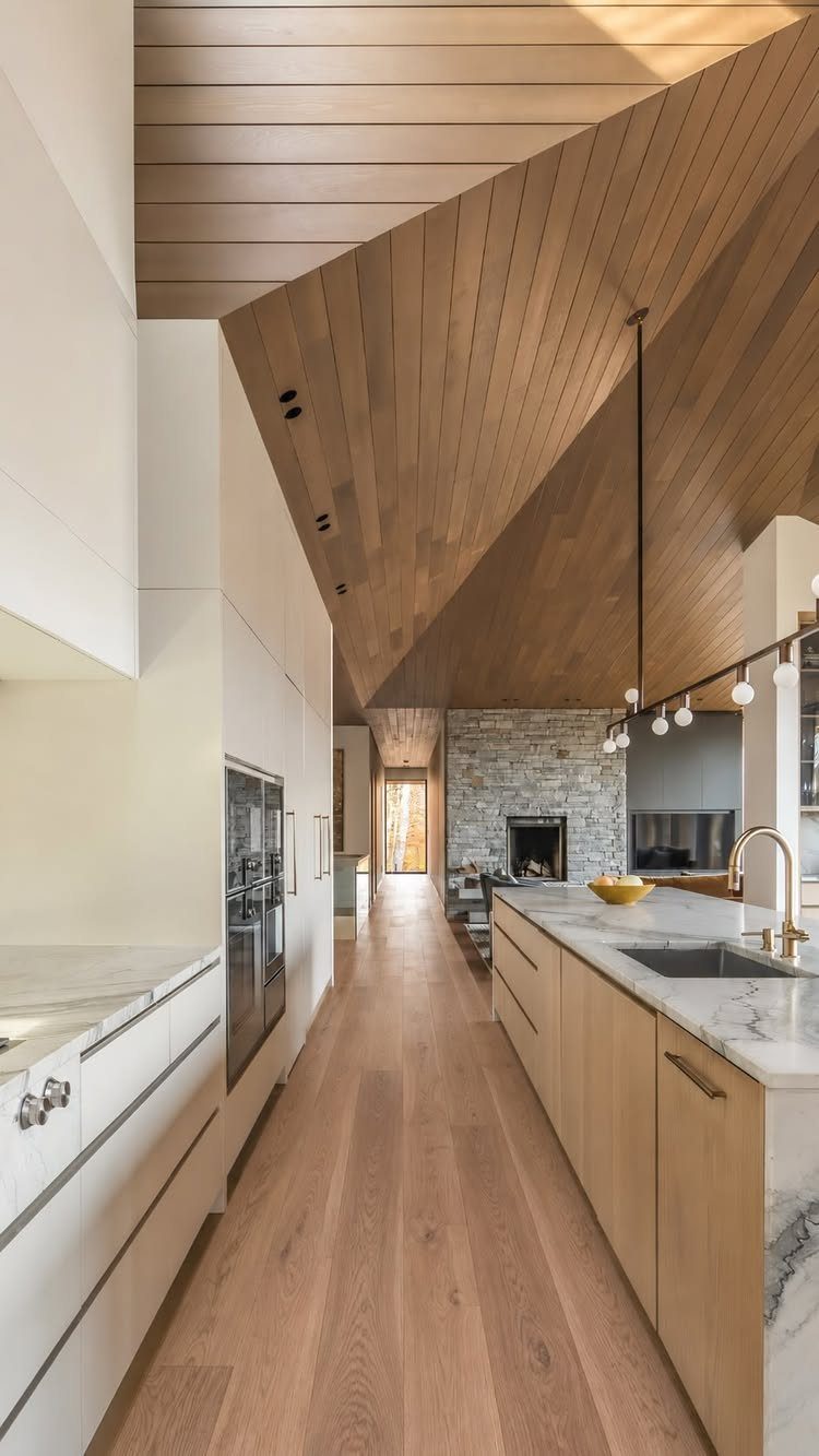 Light oak wood flooring running through a modern kitchen and living space with wooden ceilings.