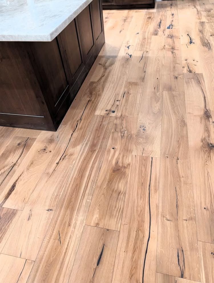 Light oak wood flooring planks with natural knots and grain patterns next to dark kitchen cabinets.