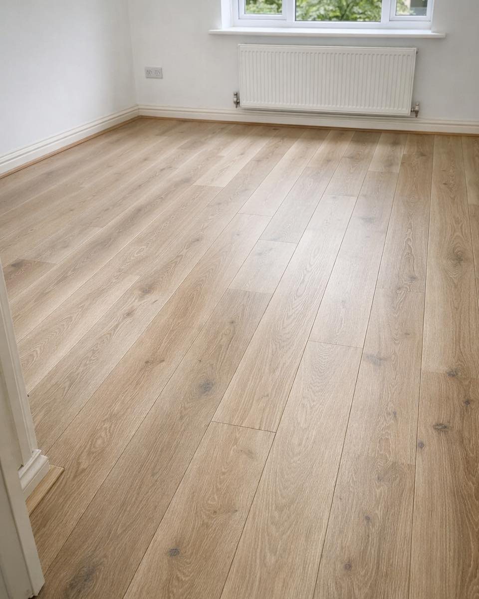Light oak wood flooring planks installed in a bright room with white walls and a radiator.