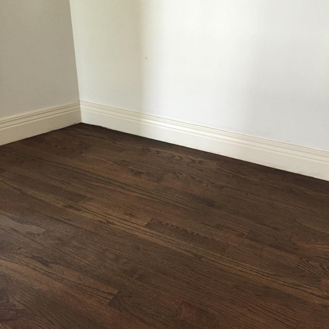 Wood Floor Colors: 5 Ideas for Every Room in 2026 6 Dark brown hardwood floor planks meeting white walls and baseboards in a room corner.