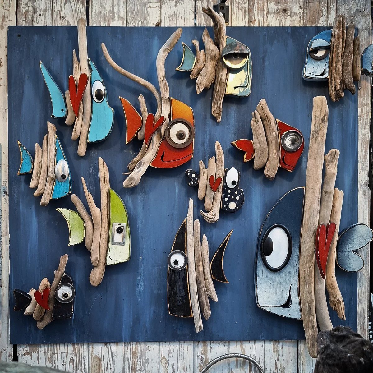 Stylized fish art made from painted scrap wood pieces on a blue wooden background.