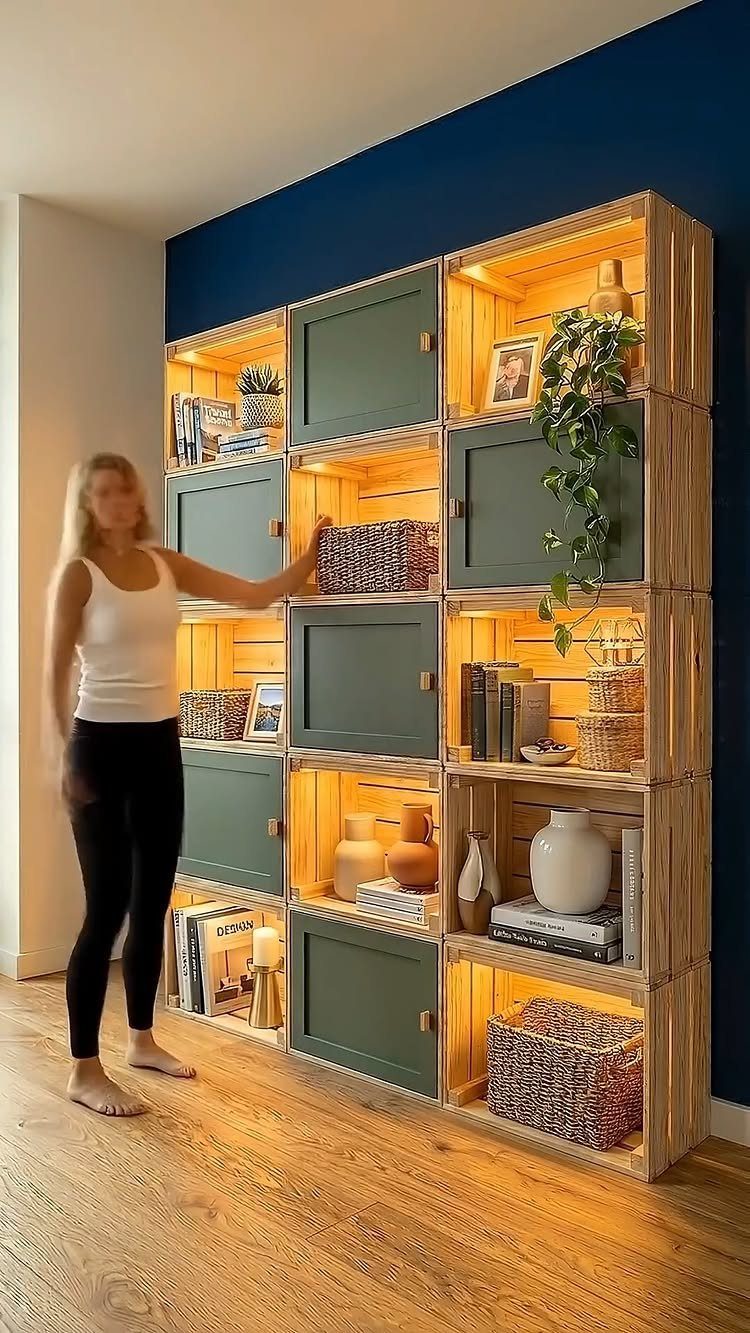 A woman stands beside a large modular shelving unit made of illuminated wooden crates.