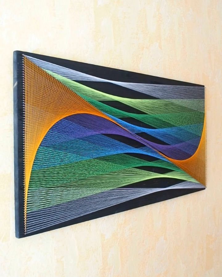 Colorful string art with flowing wave patterns stretched across a black rectangular wooden frame.