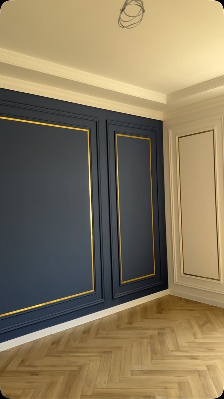 Dark blue and white walls featuring large rectangular panels with decorative gold interior trim molding.