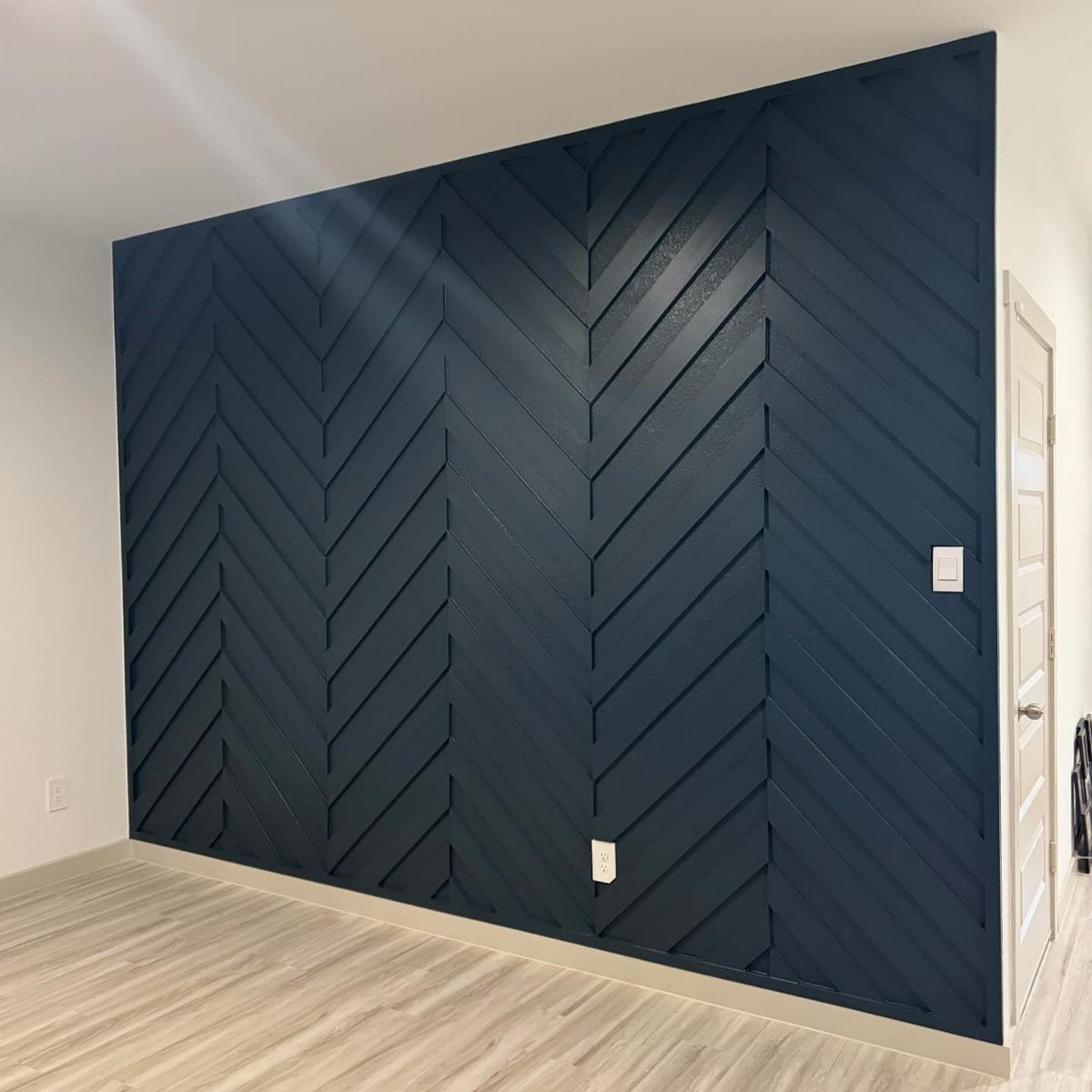 Dark navy blue wall with a geometric herringbone wood trim pattern and light wood floors.