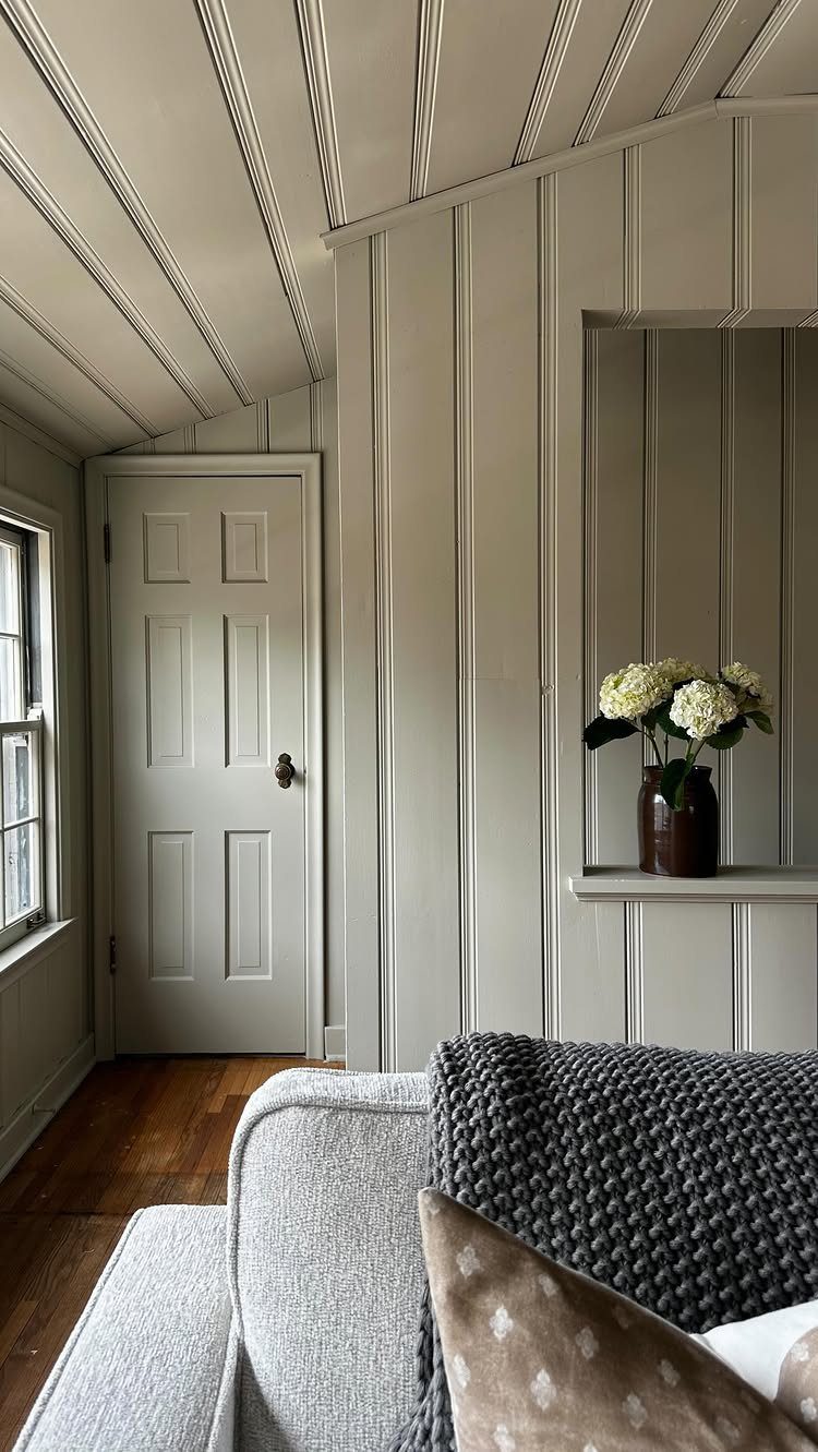 Vertical wood paneling in light grey covers the walls and ceiling of a room with a white door.