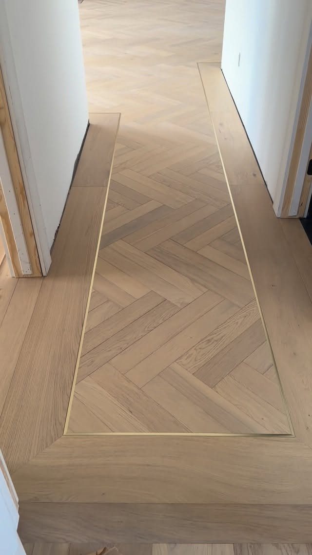 Wooden Flooring Design: 9 Ideas for Every Room 9 Light wood herringbone flooring with metallic inlay borders in a hallway between white walls.