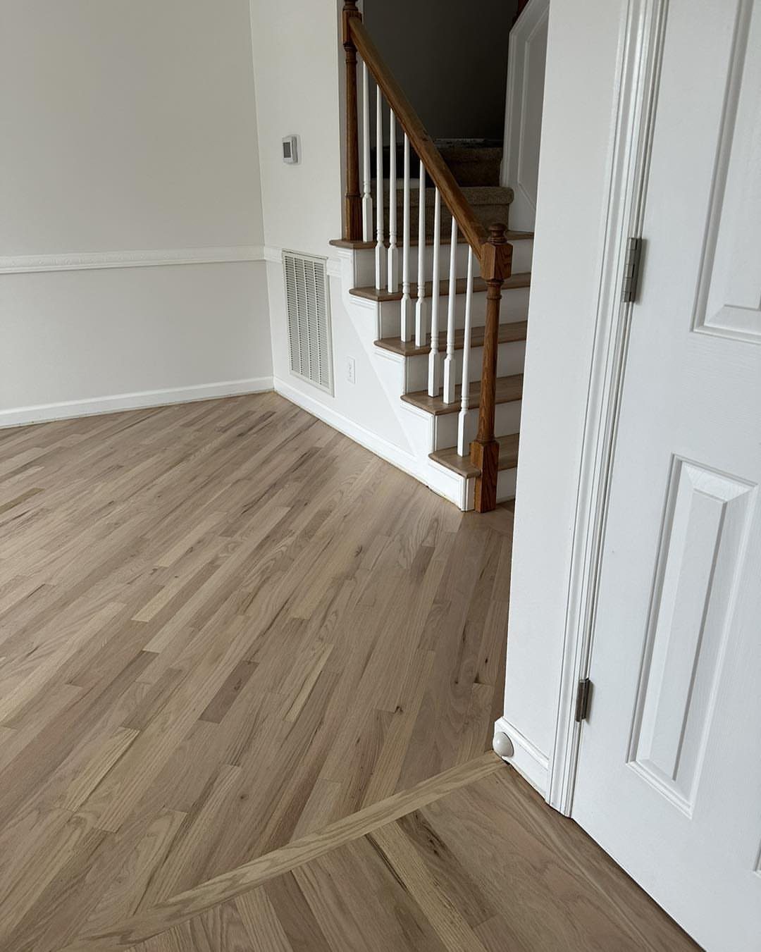 Wooden Flooring Design: 9 Ideas for Every Room 2 Light toned wooden plank flooring installed in a room next to a white door and staircase.