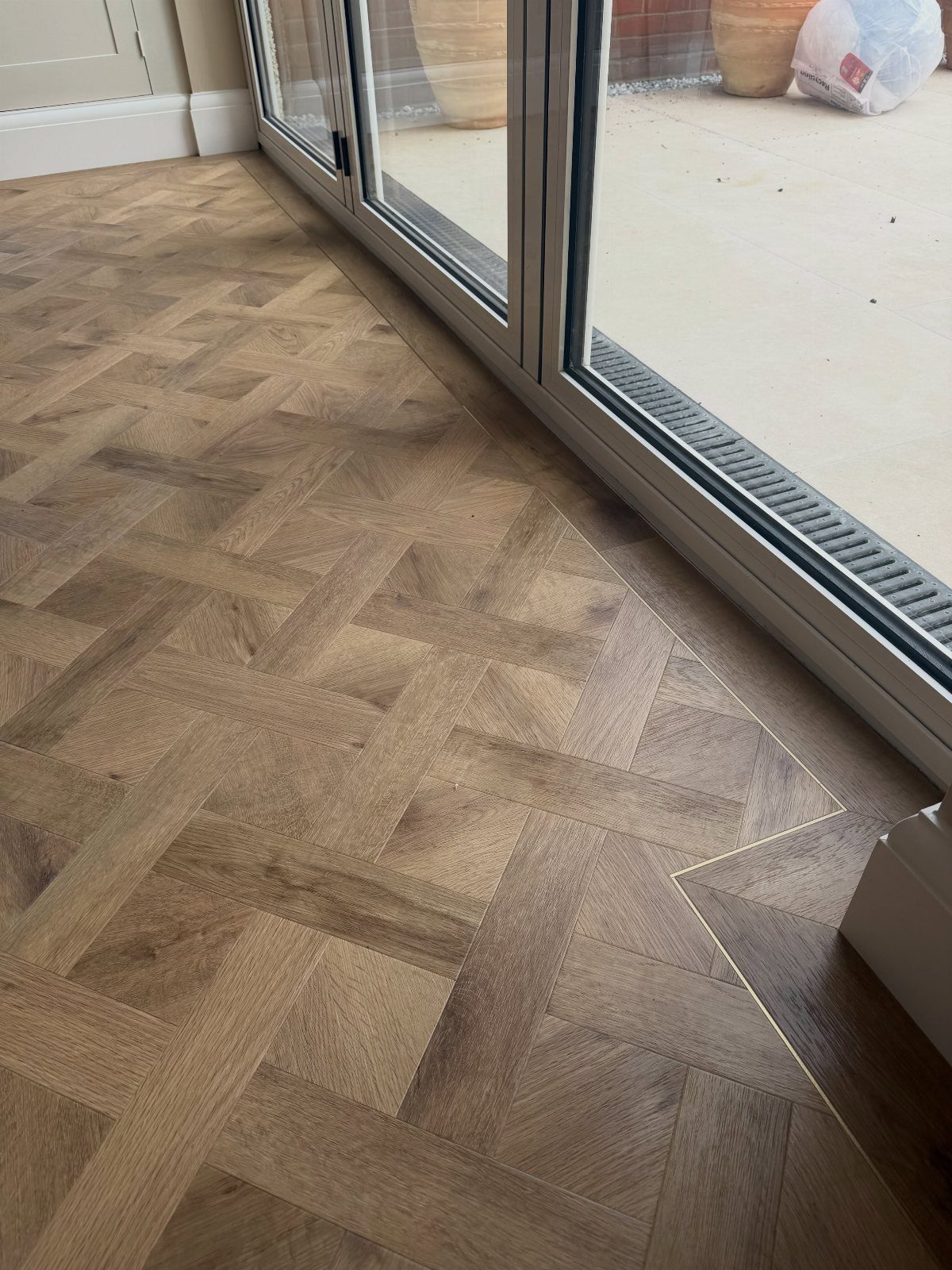 Wooden floor with a basket weave pattern laid near a sliding glass door frame.