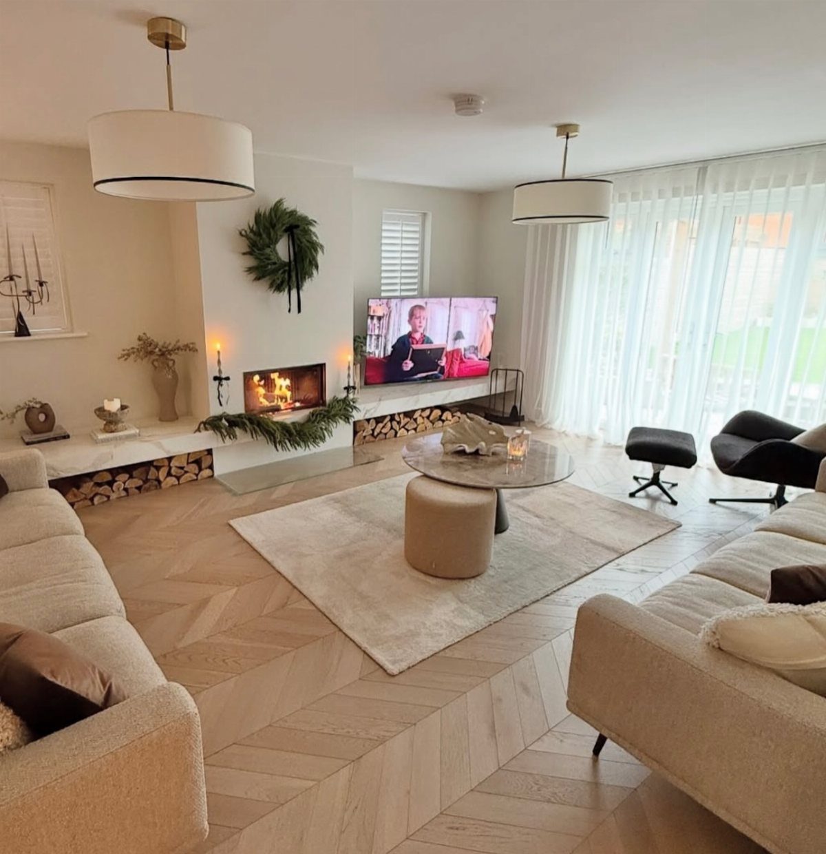 Light wood chevron flooring in a bright, modern living room with beige sofas and a fireplace.