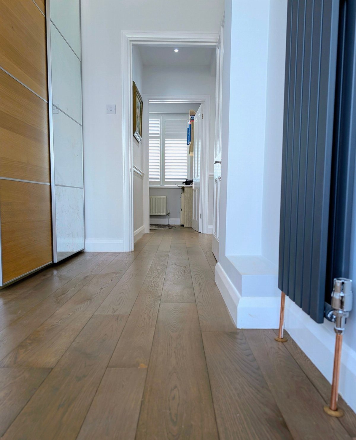 Light brown wooden floor planks running through a bright white hallway towards a window.