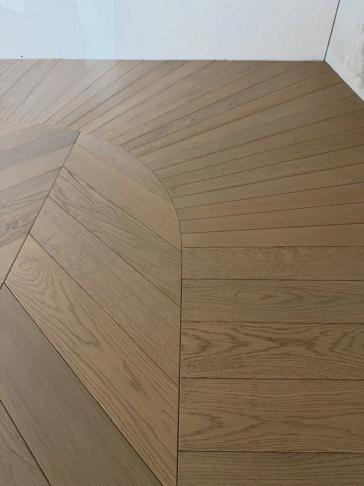 Light brown wooden floor planks arranged in diagonal and straight patterns meeting at a curved seam.