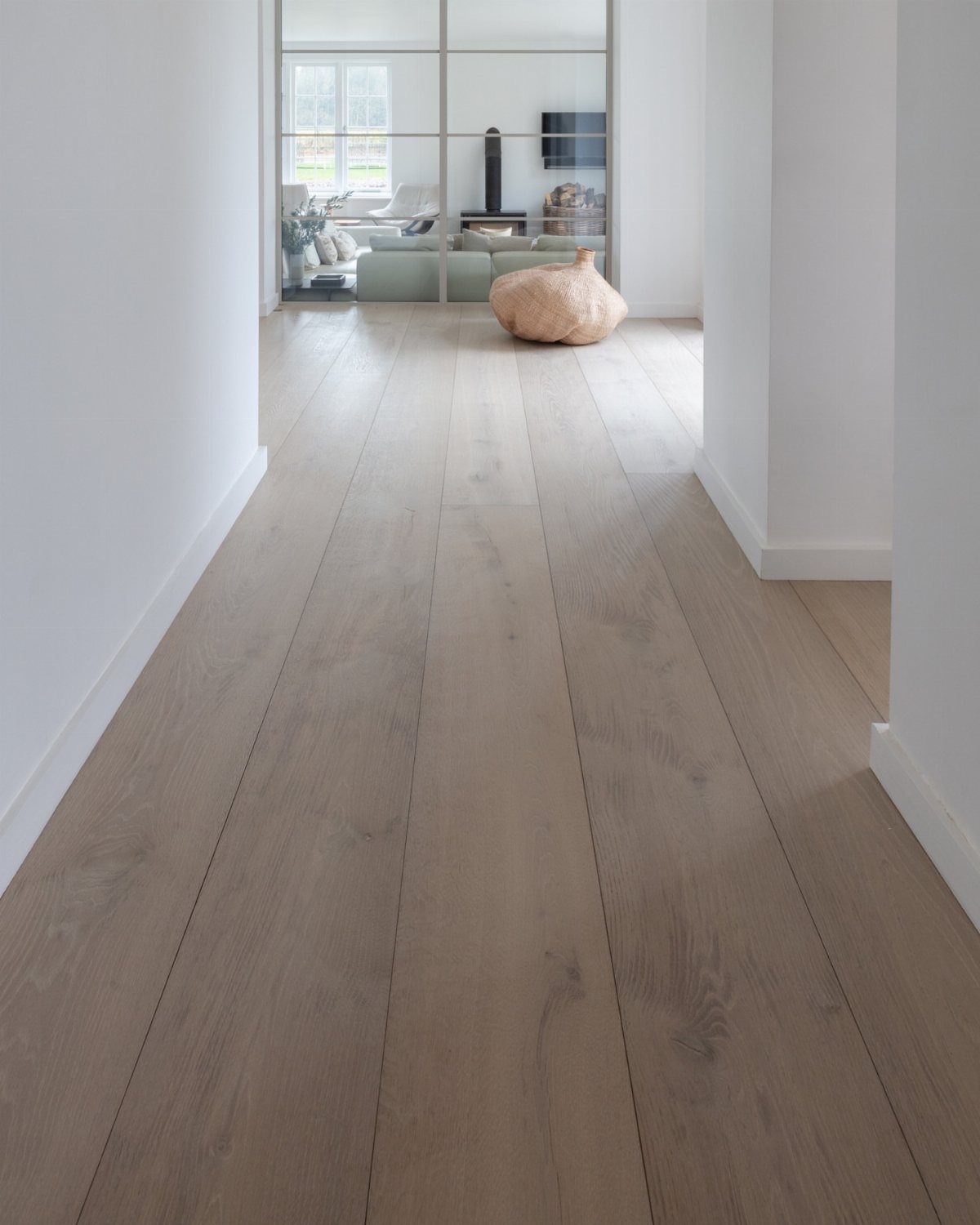 Wide light wood floor planks leading through a bright white hallway toward a living area.