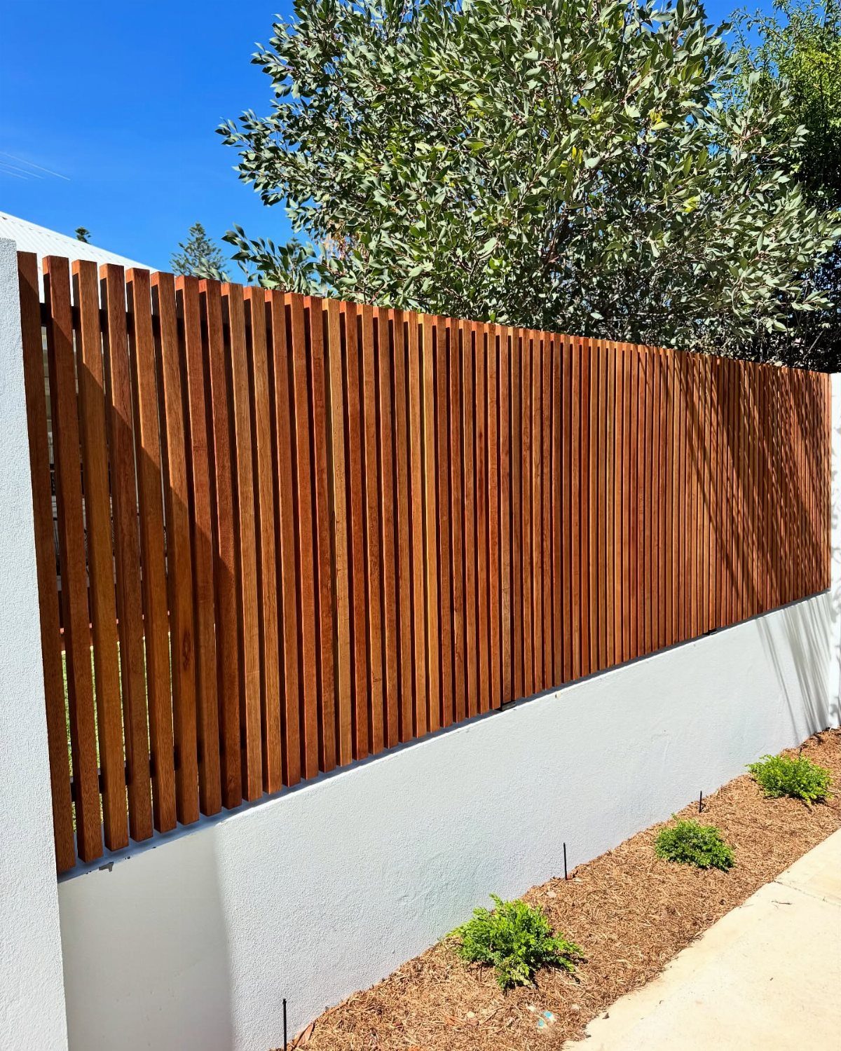 Wooden Privacy Fence: 12 Ideas That Define Your Yard 11 Vertical reddish-brown wooden slats forming a privacy fence atop a grey concrete wall.
