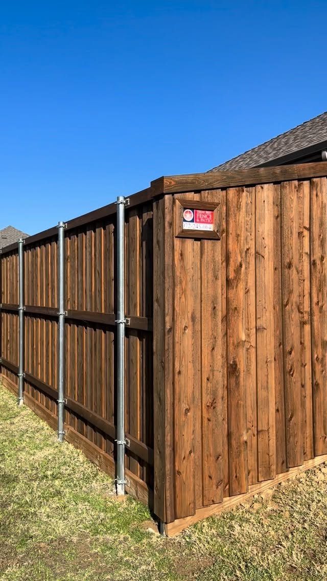 Wooden Privacy Fence: 12 Ideas That Define Your Yard 9 Dark brown wooden privacy fence with silver metal posts standing on green grass under a blue sky.